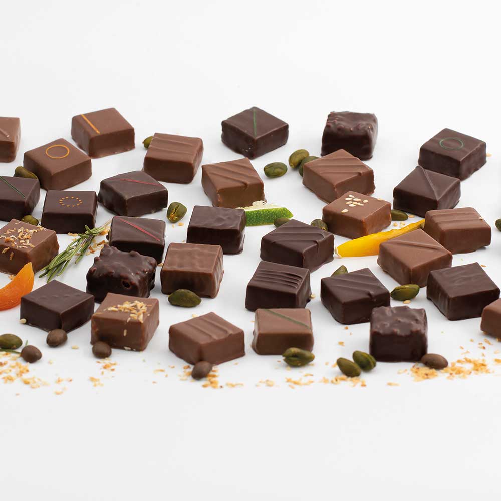 Plusieurs bouchées de chocolat noir, lait ou gourmand avec leurs ingrédients comme le sésame, le romarin ou l'abricot par l'Atelier de Thomas